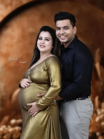 A happy and relaxed couple's portrait. The mom-to-be is glowing in her gold dress, standing with her partner for a classic maternity photo.