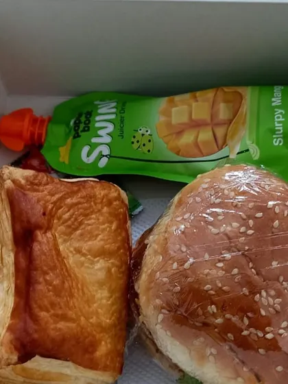 A burger, puff and mango drink sit together in one of our boxed snack combinations, ready as an individual serving.
