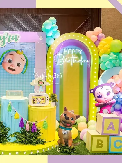 A closer look at the Cocomelon party stage, featuring JJ, his dog Bingo, and other characters, along with a rainbow arch and large ABC blocks.