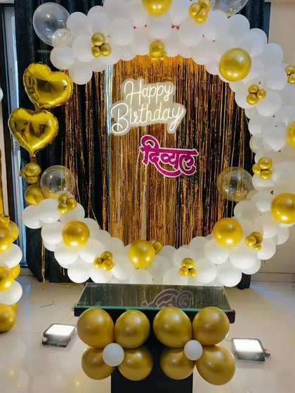 A classic first birthday decoration in white and gold. This setup includes a full balloon ring, a shimmer backdrop, a personalized name sign, and a number '1' balloon column.