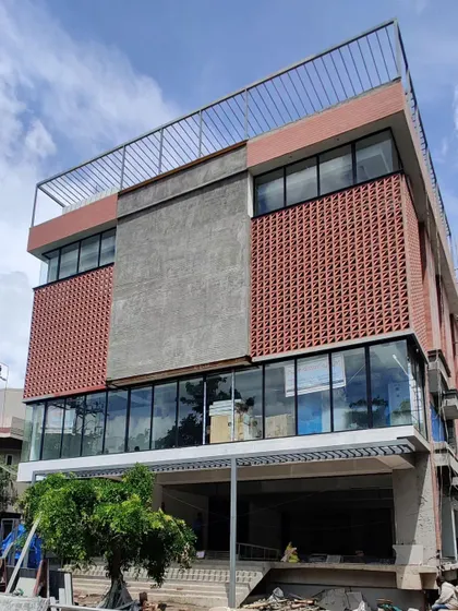 The facade combines a terracotta jali, large glass panels, and exposed concrete, creating a modern and textured exterior.