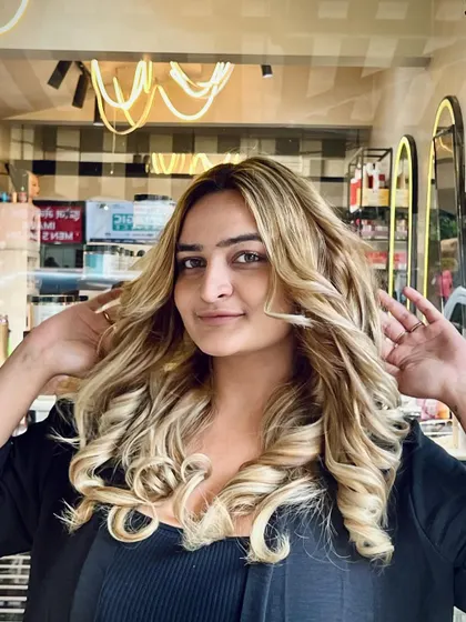 A happy client showing off the bounce and volume of her new blonde hair. The curls are perfectly formed and full of life.