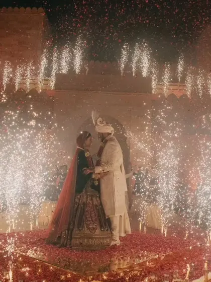 A wide shot capturing the sheer scale of the celebration, with the couple at the center of a dazzling cold pyro display against the magnificent backdrop of Suryagarh fort. It's a moment of pure, unadulterated magic.