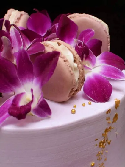 A close-up of the fresh orchids and macarons on the tropical pineapple cake. The vibrant purple of the flowers contrasts beautifully with the soft lavender buttercream.
