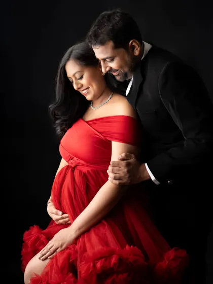 A close-up shot capturing the love and excitement. The vibrant red of her off-the-shoulder gown contrasts beautifully with his classic suit, making for a very romantic and formal couple's portrait.