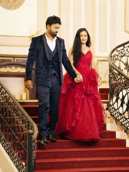 A candid moment of the couple walking hand-in-hand. The combination of the red gown and blue velvet suit is both bold and romantic, ideal for a grand setting.