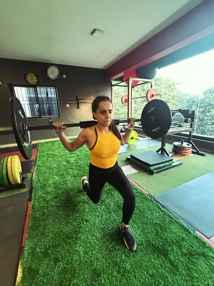A client performs a walking lunge with a barbell on her back, a tough but effective full-body challenge.