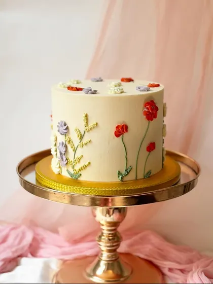 A minimalist cake with delicately piped wildflowers and leaves. The simple arrangement on a smooth buttercream canvas creates a look of rustic elegance.