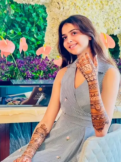 A happy client with her personalized mehndi, featuring her and her partner's initials on the palms.
