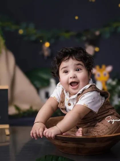 A joyful 9-month milestone shoot with a fun jungle safari theme. This little boy's excited expression is priceless as he sits in a wooden bowl, surrounded by friendly lion and giraffe props.