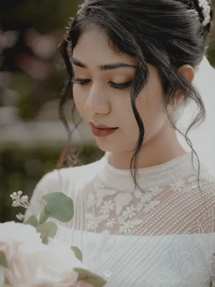 A delicate close-up of a bride in her white lace gown, looking down at her bouquet.