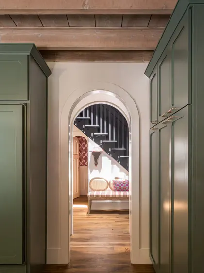 An arched doorway in the Saratoga home creates a beautiful, soft transition between spaces. This view from the kitchen looks towards the main staircase, showcasing how architectural details can frame moments and guide the eye through the home.