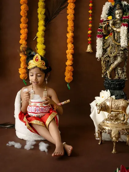 A solo portrait of a young girl dressed as Krishna, enjoying a pot of butter.