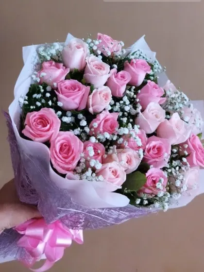 A beautiful hand bouquet of pink roses and baby's breath, wrapped in delicate paper with a matching pink bow. A timeless gift for any occasion.