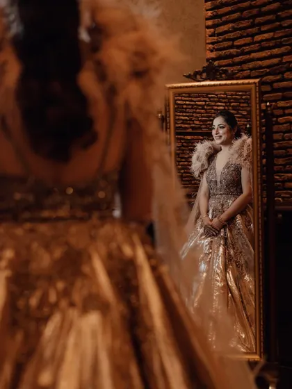 A beautiful reflection shot of the bride looking in the mirror before her reception, her glamorous feathered gown creating a stunning silhouette.