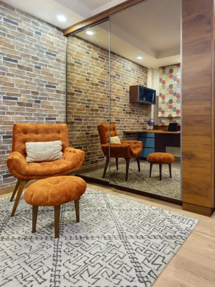 The walk-in closet was reimagined as a versatile den. The space combines a home office, reading nook, and storage, with an exposed brick wall and large mirrors creating an illusion of depth.