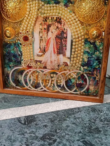 A side view of a custom wedding ornament frame. This piece includes preserved orchid flowers, kaleere, chooda, and a pearl mala, all encased in a beautiful wooden box frame.
