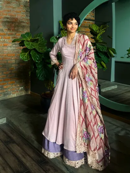 This Anarkali suit with a layered palazzo and a hand-painted dupatta is an exquisite ensemble that ensures you radiate beauty on every occasion.
