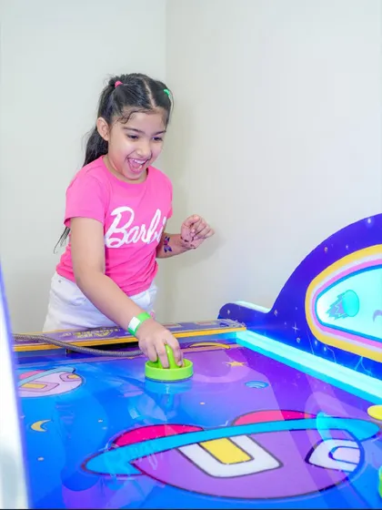 A girl celebrates a point while playing air hockey with friends.
