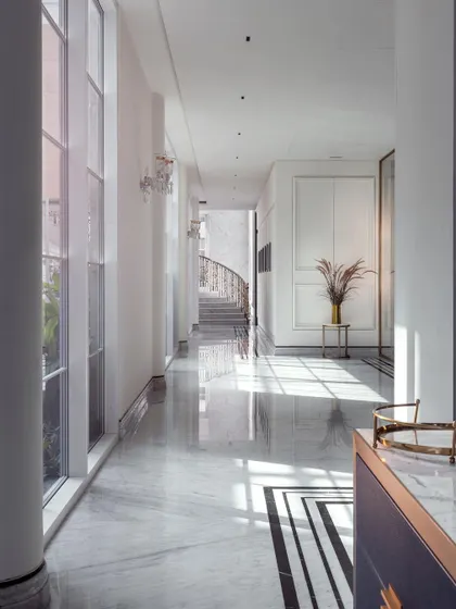 A long, sun-drenched corridor in The Grand Alabaster, with light pouring in from tall windows. The gleaming marble floor reflects the light, enhancing the sense of space and creating a pathway of pure elegance.