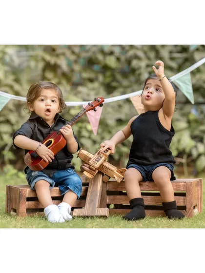 A duplicate of image 3, this photo shows the twins engaged in playful activities, one with a ukulele and the other with a toy plane, highlighting a fun, themed setup.