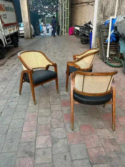 A set of three mid-century modern armchairs with cane backrests and black leatherette seats. The brass-capped legs add a touch of luxury.