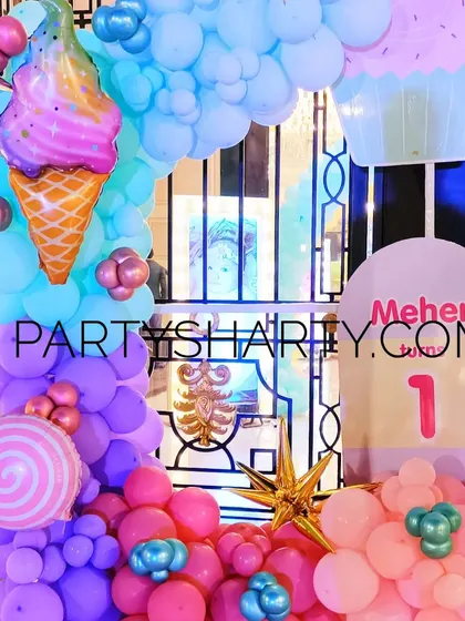A close-up of a candy-themed balloon arch, featuring large foil balloons shaped like ice cream, cupcakes, and lollipops.