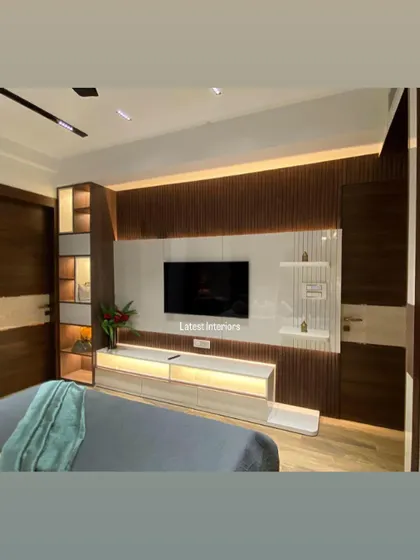 The TV unit in this bedroom features a combination of wooden fluting and high-gloss white panels with backlighting. The design is modern, functional, and visually interesting.