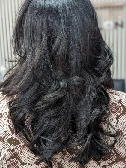 A final look at a layered haircut finished with a bouncy blowout. The curls are shaped away from the face to create volume and movement, resulting in a classic and elegant hairstyle suitable for any occasion.