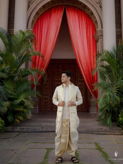The groom standing proudly in his wedding dhoti before a dramatic red curtain entrance.