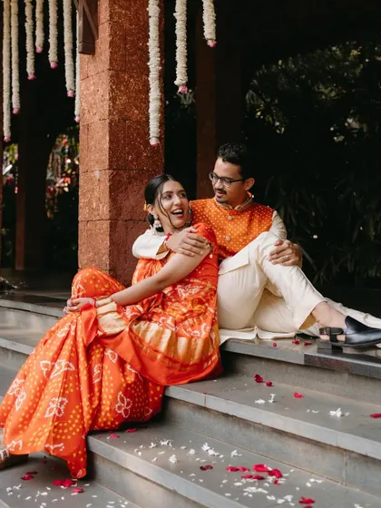 A relaxed and happy portrait of a couple sitting on steps after their Haldi ceremony, sharing a candid moment of conversation.