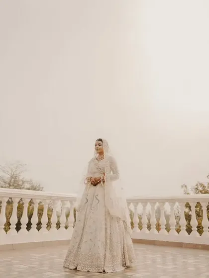 An ethereal portrait of the bride on a white balcony, her elegant lehenga standing out against the misty, atmospheric background.