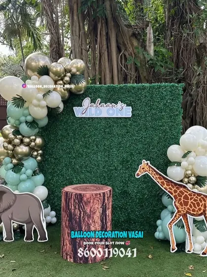 A "Wild One" jungle theme for an outdoor party. This setup features a grass wall backdrop, an elegant balloon garland, and realistic elephant and giraffe cutouts.