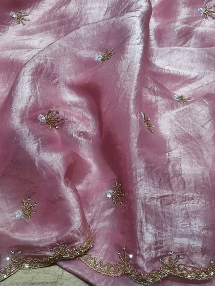 A close-up of a pink crush tissue saree with delicate, sparkling embroidery. The fabric has a lovely sheen and a soft, crushed texture that makes it unique and easy to drape.
