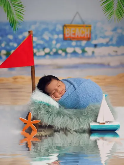 A creative beach-themed newborn shoot. The baby is sleeping soundly by the "water," complete with a miniature sailboat and a beach backdrop.