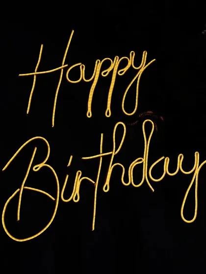 A close up of a custom 'Happy Birthday' neon sign in a warm yellow glow. These signs are a popular add on for creating a focal point at any celebration.