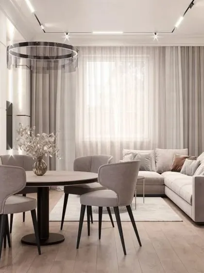 The living area in this open-plan space is designed for comfort, with a plush L-shaped sofa and soft, sheer curtains that diffuse natural light. The track lighting on the ceiling provides flexible illumination for the entire room.