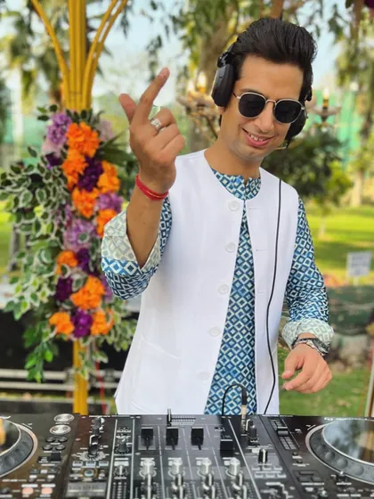 A playful moment behind the decks at a sunny outdoor event. The mood is happy, the music is flowing, and the floral decor adds to the beautiful sundowner vibe.