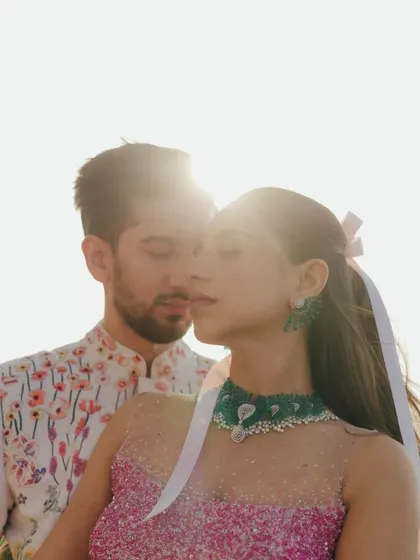 A sun-drenched, intimate portrait from a carnival-themed event. The close-up captures the couple's connection, with the bright light creating a dreamy, romantic haze.