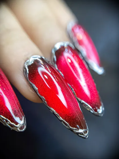 A close-up of fiery red cat-eye nails with a unique 3D silver chrome border. This design is perfect for making a bold statement during festive seasons.