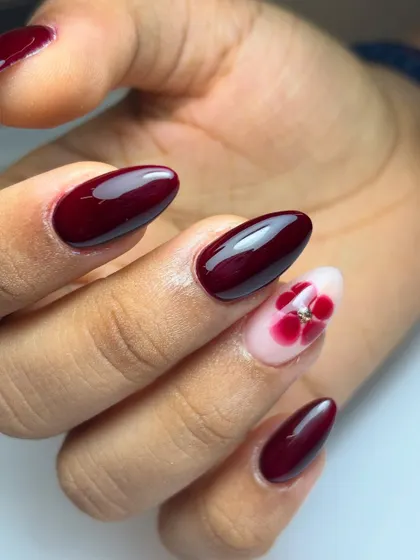 This angle highlights the glossy finish of the berry red nails and the delicate gem at the center of the floral accent.