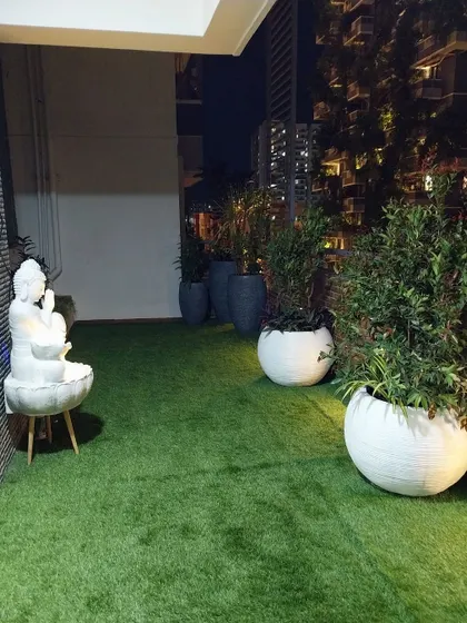 This terrace garden is designed for evening ambiance. Artificial turf, large white planters, and a serene Buddha statue are strategically lit to create a peaceful and meditative space at night.