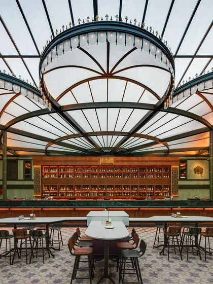 The heart of Jollygunj, the grand central bar. The custom-designed, canopy-like light fixtures are the focal point, illuminating the patterned floor tiles and extensive back bar. This element was crucial to the project's narrative, evoking the charm and grandeur of a bygone era.