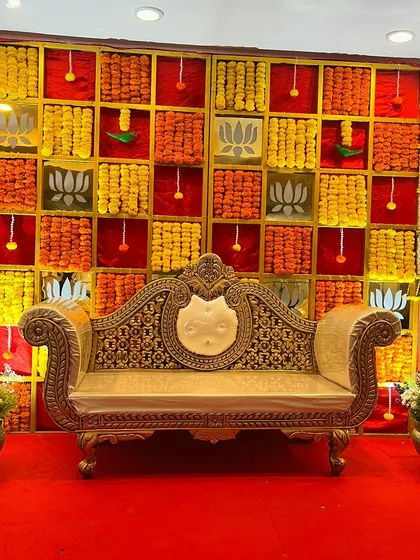 A vibrant and colorful backdrop for a baby shower, using panels of orange and yellow marigolds. The design is accented with lotus motifs and red fabric for a rich, traditional feel.
