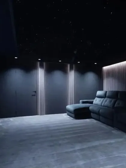A sleek, modern theater with a large sectional sofa, perfect for sprawling out during a movie marathon. The dark walls and carpet help the screen's image stand out.