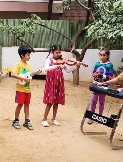 A small band of young musicians performs for the school during our Christmas celebration. They play the ukulele, violin, and keyboard, sharing their talents and filling the air with music.