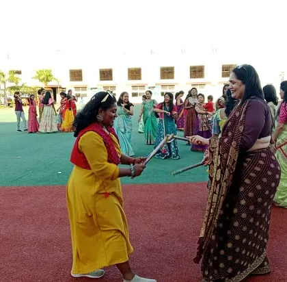 A teacher and a student enjoy a moment of shared fun, dancing together with dandiya sticks.