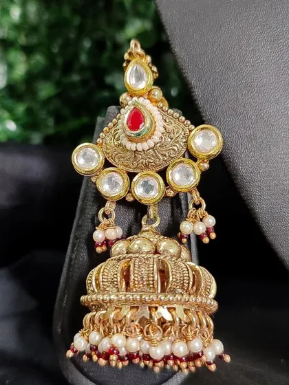 A traditional temple-style jhumka with a crown-like design. This rental earring features kundan work, a central red stone, and pearl drops.