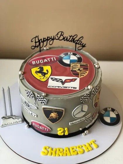 A cake for a true car enthusiast, decorated with the logos of famous luxury car brands like Ferrari, BMW, and Lamborghini.
