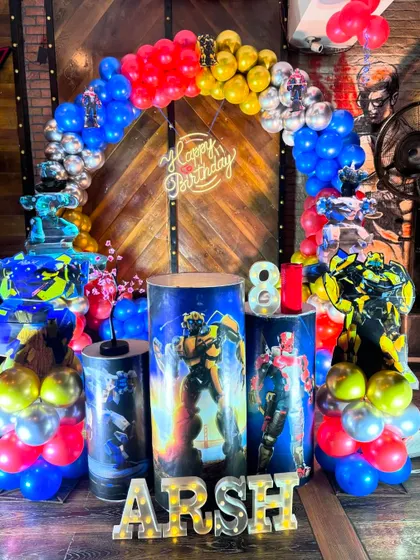 An action-packed Transformer theme for an 8th birthday. The decor features a balloon arch in primary colors and pedestals wrapped with images of the robot characters.